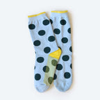 The Hooray Sock Co. Clipper Sock is a unisex crew sock in light blue with large black polka dots, yellow cuffs, heels, and toes, shown overlapping on a plain light background.