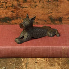 The HomArt Terrier Door Wedge, Cast Iron in Antique Brown, shaped like a dog, rests atop a closed red book on a rustic wooden background.