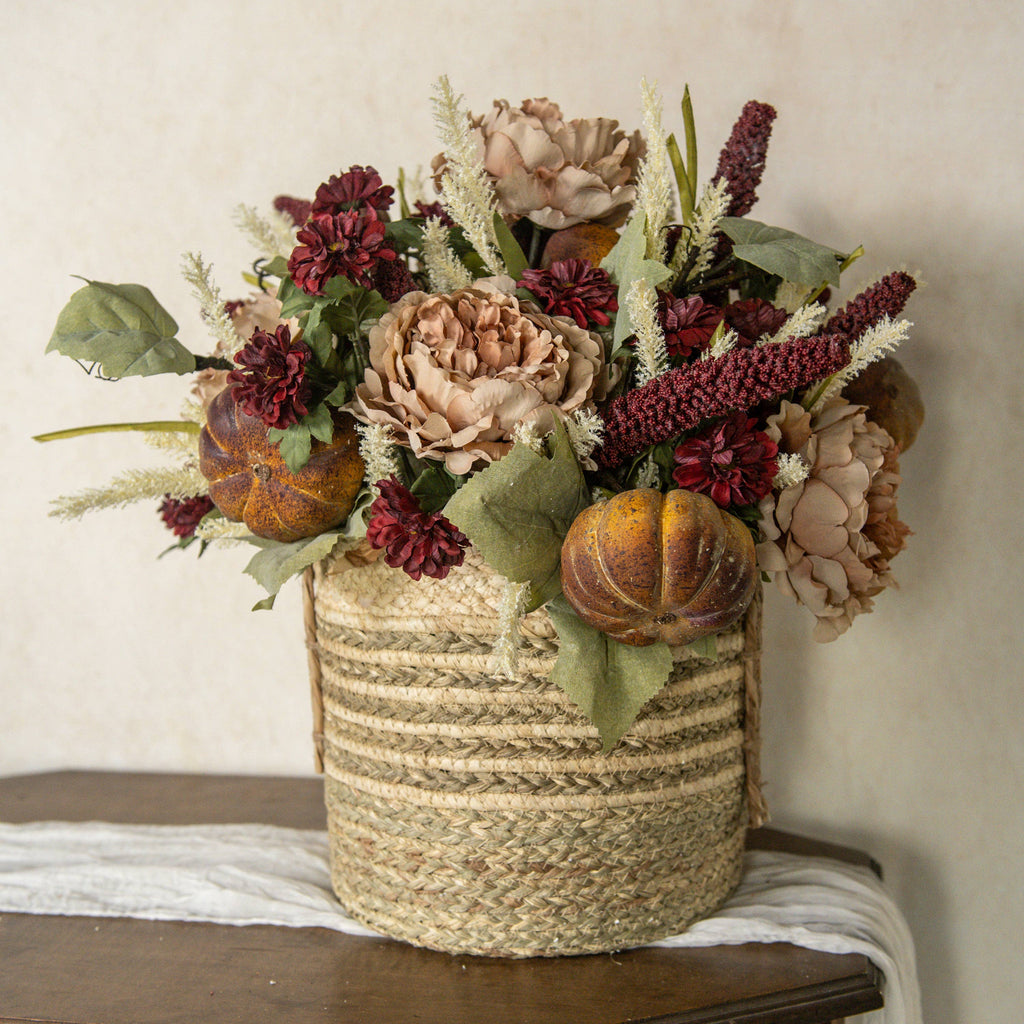 A 31" BURGUNDY SORGHUM SPRAY by Ragon House is arranged with autumn florals, pumpkins, peonies, and green leaves in a rustic basket on a wooden surface against a neutral background.