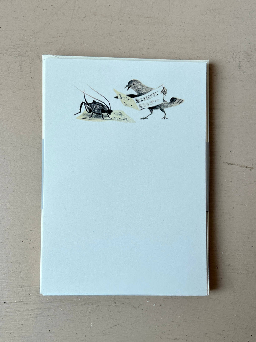 The Music Lessons Mini Stationery Set by Parcel includes 8 notepads on creamy white cardstock, each featuring a cricket playing violin and a bird with sheet music on a blank background.