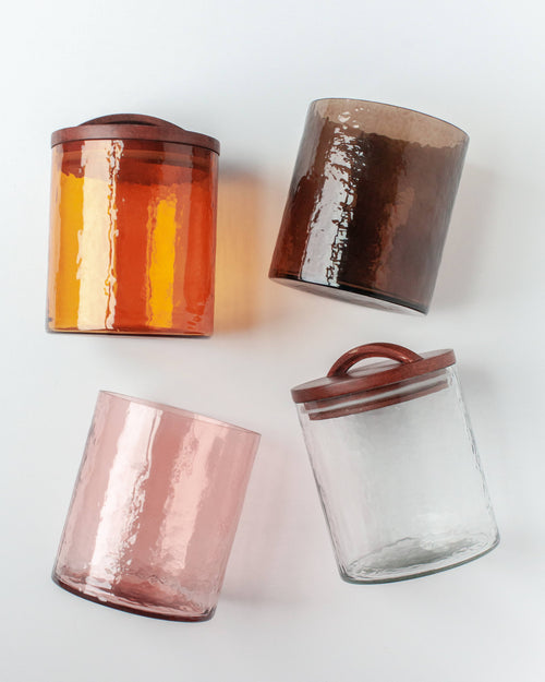 Four Handblown Hammered Glass Canisters: Smoke / Small by Creative Women are displayed diagonally on a white surface, each featuring a hand-carved wooden lid for an airtight seal.