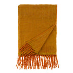 The Indaba Trading Oslow Wool Blend Throw in Turmeric is folded with fringe tassels on a white background. One corner is flipped to reveal both sides of this cozy, textured blanket.
