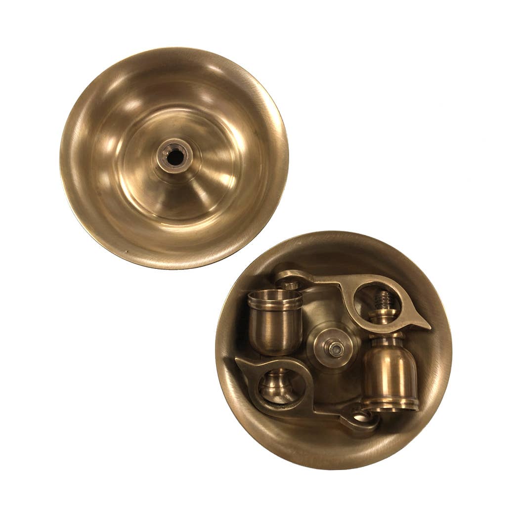 Shown are two round brass items: one is an empty, shallow bowl with a central hole; the other holds metal parts inside. Both are Madison Bay Co. Brighton Bun Traveling Chamberstick Sets, inspired by antique designs, displayed on a white background.