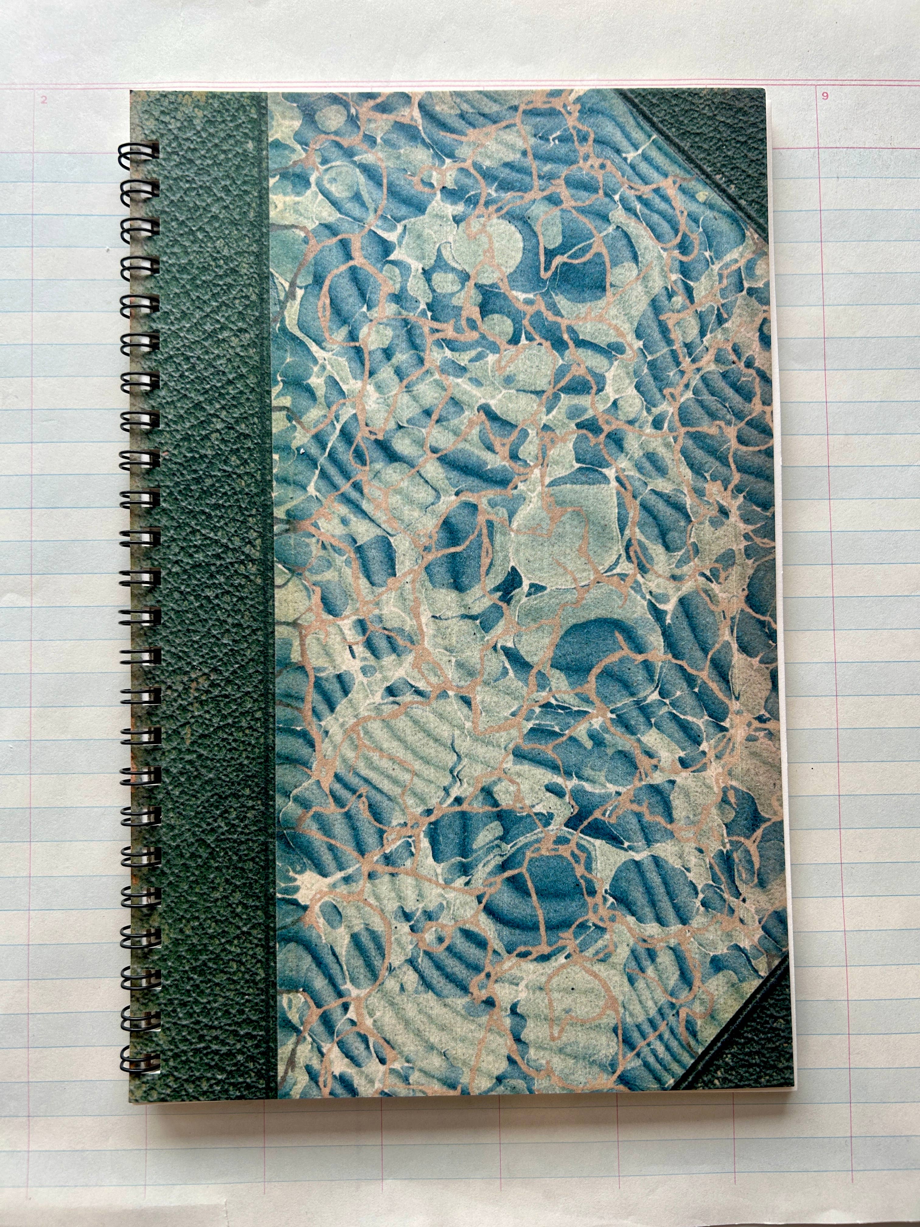 The Parcel Antique Endpaper Notebook: Large - Blue & Burgundy / Unlined features a marbled blue, white, and beige cover with a green textured spiral binding and corners, resembling vintage high-quality card stock.