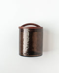 The Handblown Hammered Glass Canisters: Smoke / Small by Creative Women features translucent brown recycled glass with a textured finish and a dark hand-carved wooden lid, set against a plain white background.