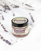 A jar of Roots And Leaves Magnesium Body Butter with a vintage-style label rests on a white surface, surrounded by dried lavender, emphasizing its role as a sleep aid and for boosting magnesium absorption.