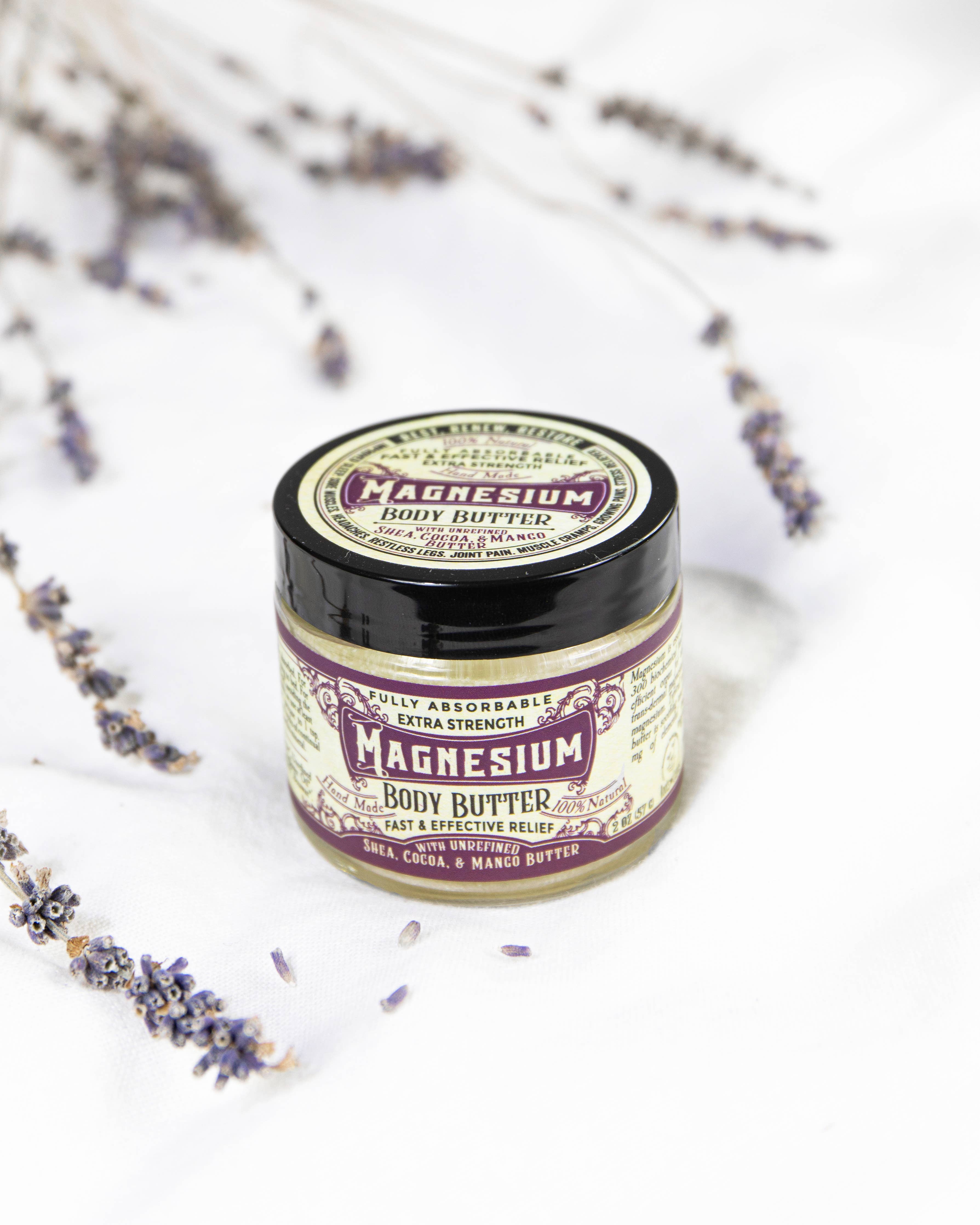 A jar of Roots And Leaves Magnesium Body Butter with a vintage-style label rests on a white surface, surrounded by dried lavender, emphasizing its role as a sleep aid and for boosting magnesium absorption.