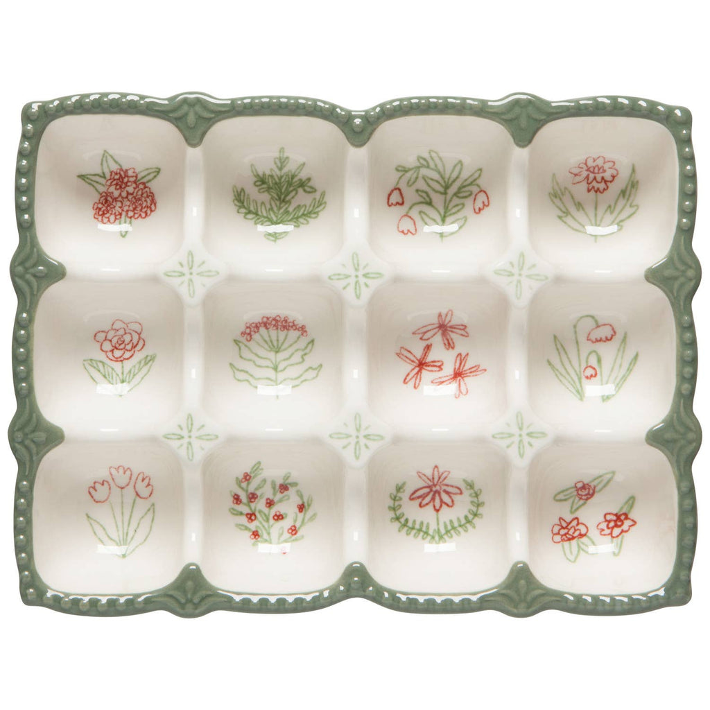 The Camellia Egg Holder by Danica Heirloom is a stoneware crate with green edges and twelve sections, each adorned with red or green hand-drawn flowers, leaves, or dragonflies—ideal for a charming kitchen display.