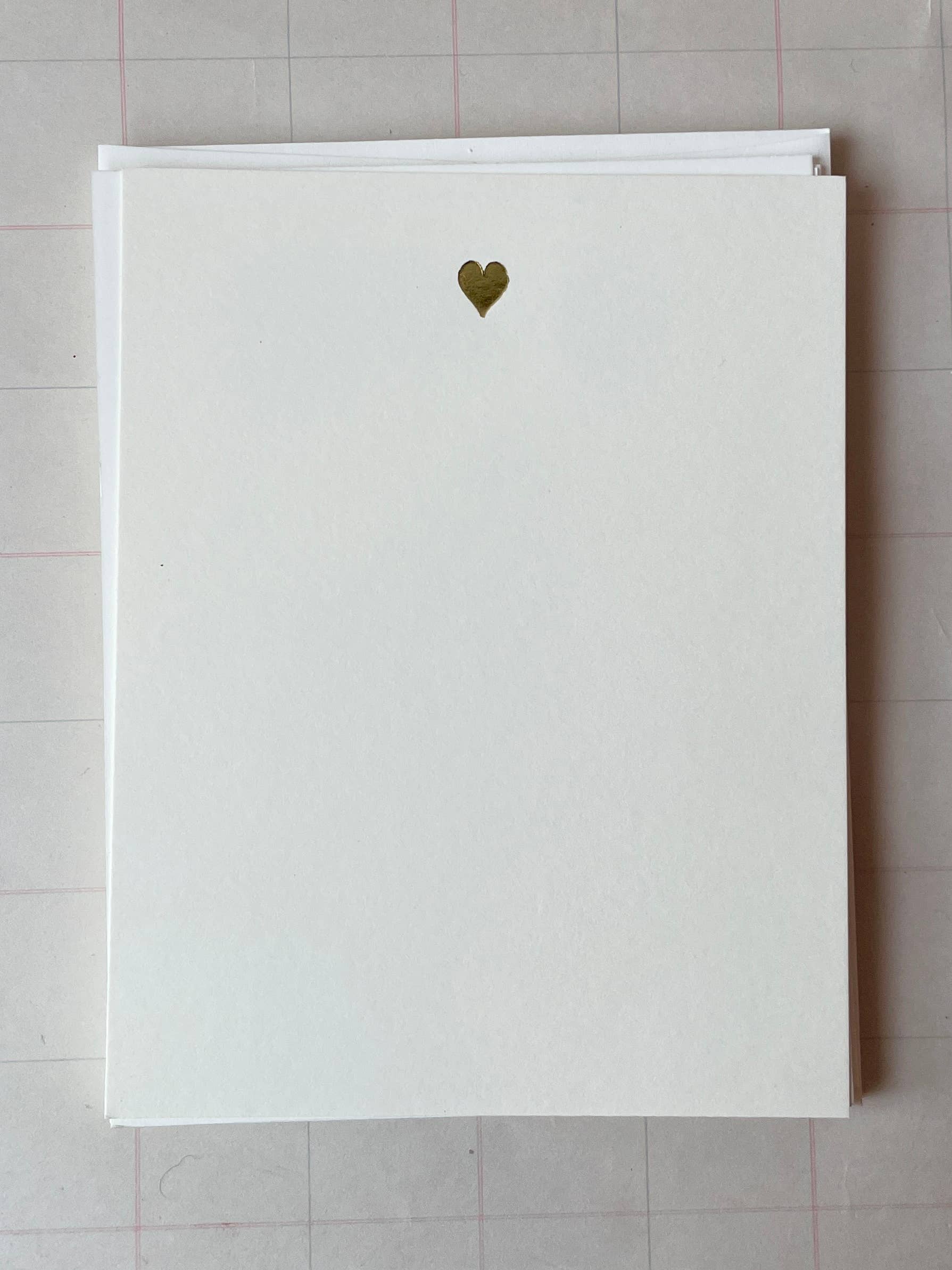 A square white Parcel card ("Tiny Heart: Silver") with a small silver foil heart near the top sits atop another white card on a light grid-patterned surface.