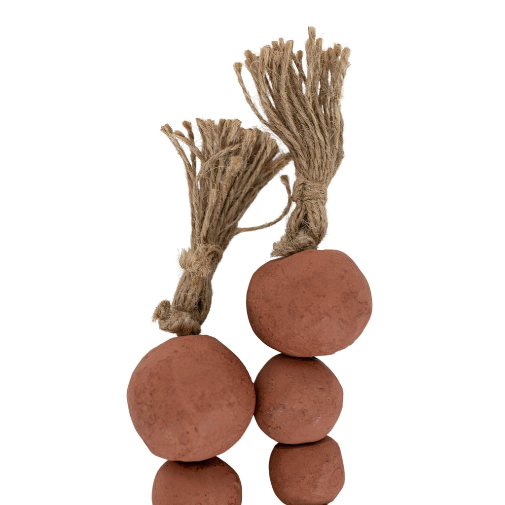 Foreside Home & Garden’s Clay Garland Terracotta + Jute features two artisan-made, reddish-brown clay balls with rough surfaces, each topped with a rustic terracotta-twined jute strand for a tassel-like look.