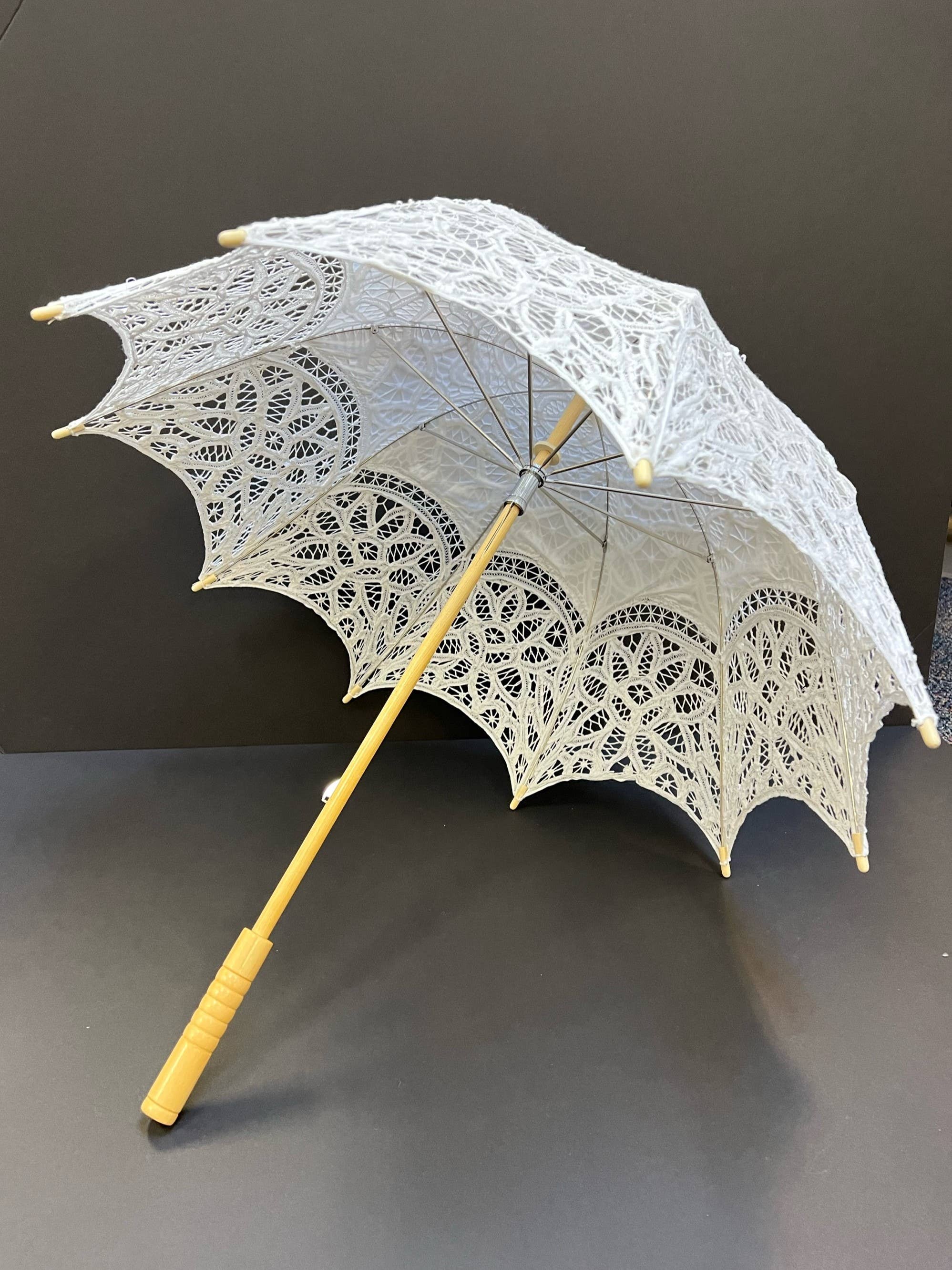 The Parasol - White by Peking Handicraft is a Battenburg Victorian parasol with intricate lace, light wooden handle and frame, displayed open against a dark background—an elegant accessory for any occasion.