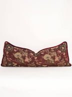The Tapestry Long Lumbar by Twenty Third by Deanne is a rectangular jacquard pillow with a dark red background and vintage floral patterns in muted green, pink, and beige on a plain white backdrop.