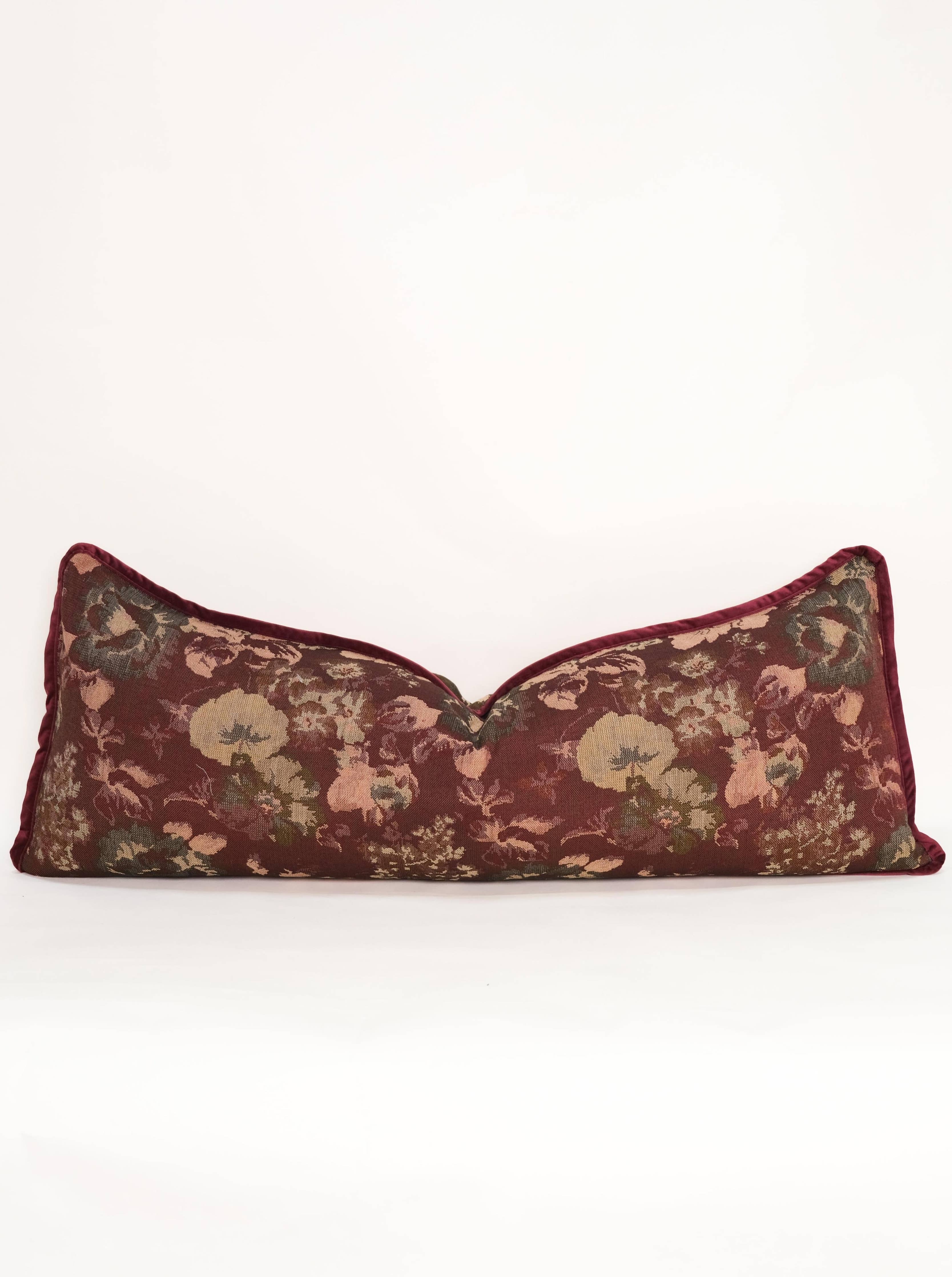 The Tapestry Long Lumbar by Twenty Third by Deanne is a rectangular jacquard pillow with a dark red background and vintage floral patterns in muted green, pink, and beige on a plain white backdrop.
