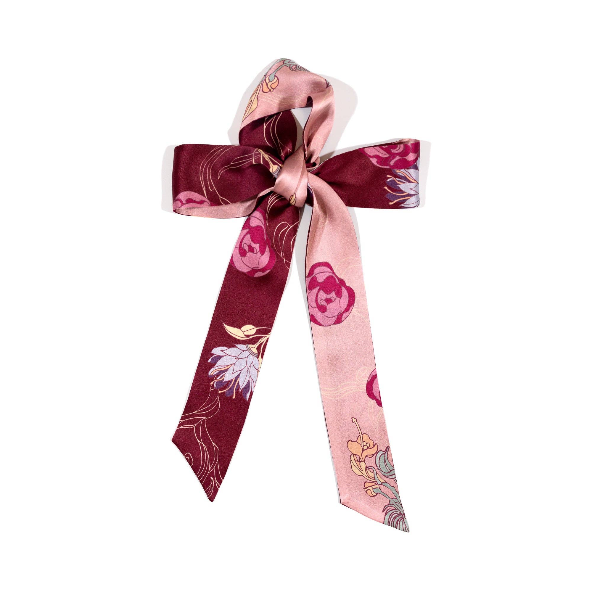 The Silk Skinny Scarf - Ruby Red by Lost Pattern NYC features pink and burgundy floral patterns with long ribbon tails and a smooth, shiny finish, making a charming hair accessory or headband, shown on a white background.