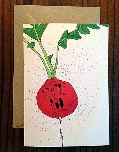 The Pen+Pine You’re Rad Card features a red radish with green leaves and "You're rad" on the front. This eco-friendly card is blank inside, comes with a brown envelope, and is shown on a wooden surface.