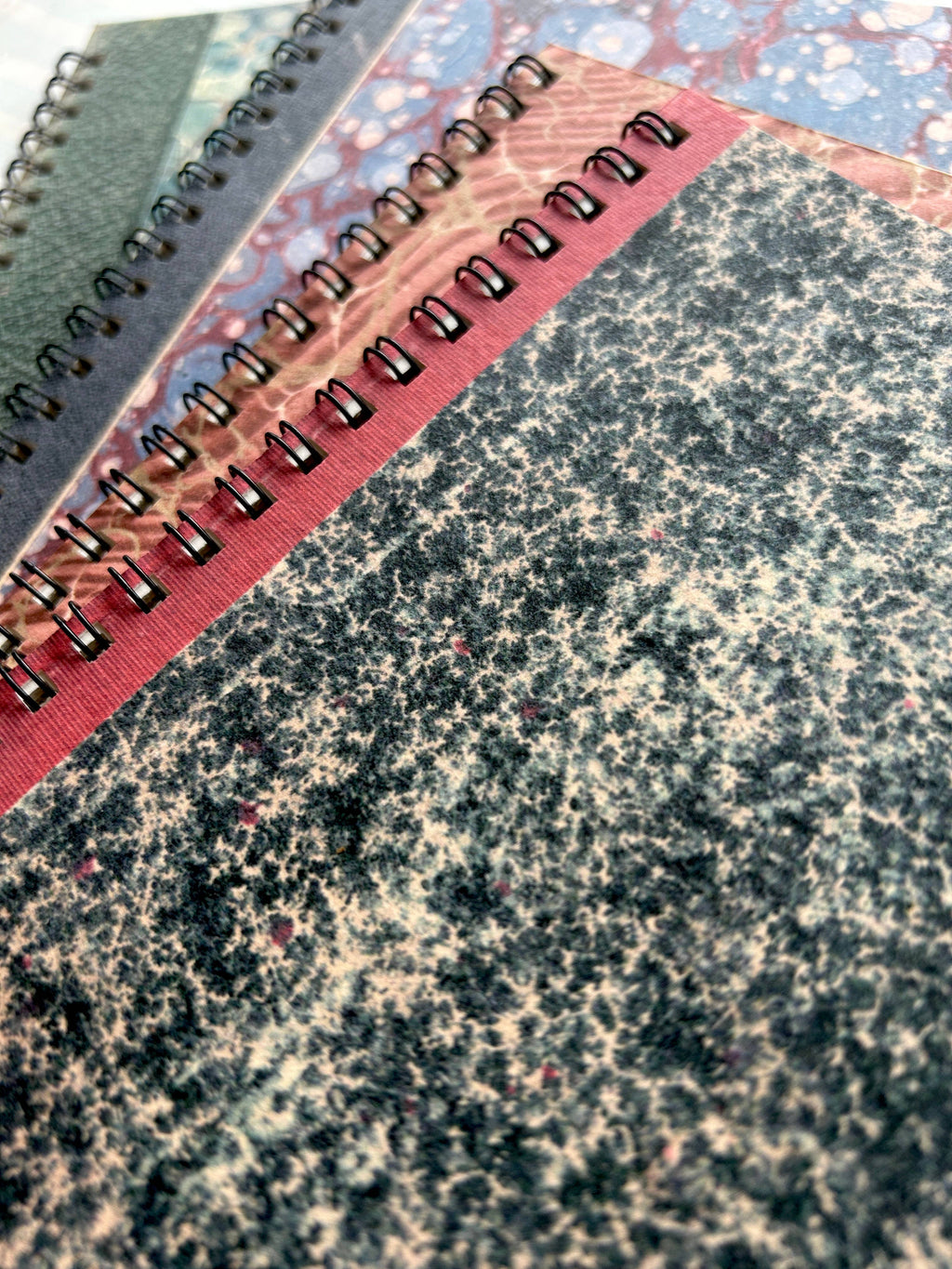Four Parcel Antique Endpaper Notebooks (Small, Composition, Unlined) with vintage marbled covers in different colors are fanned out beside a 5x7 card, showing off the unique textures and patterns of each cover.