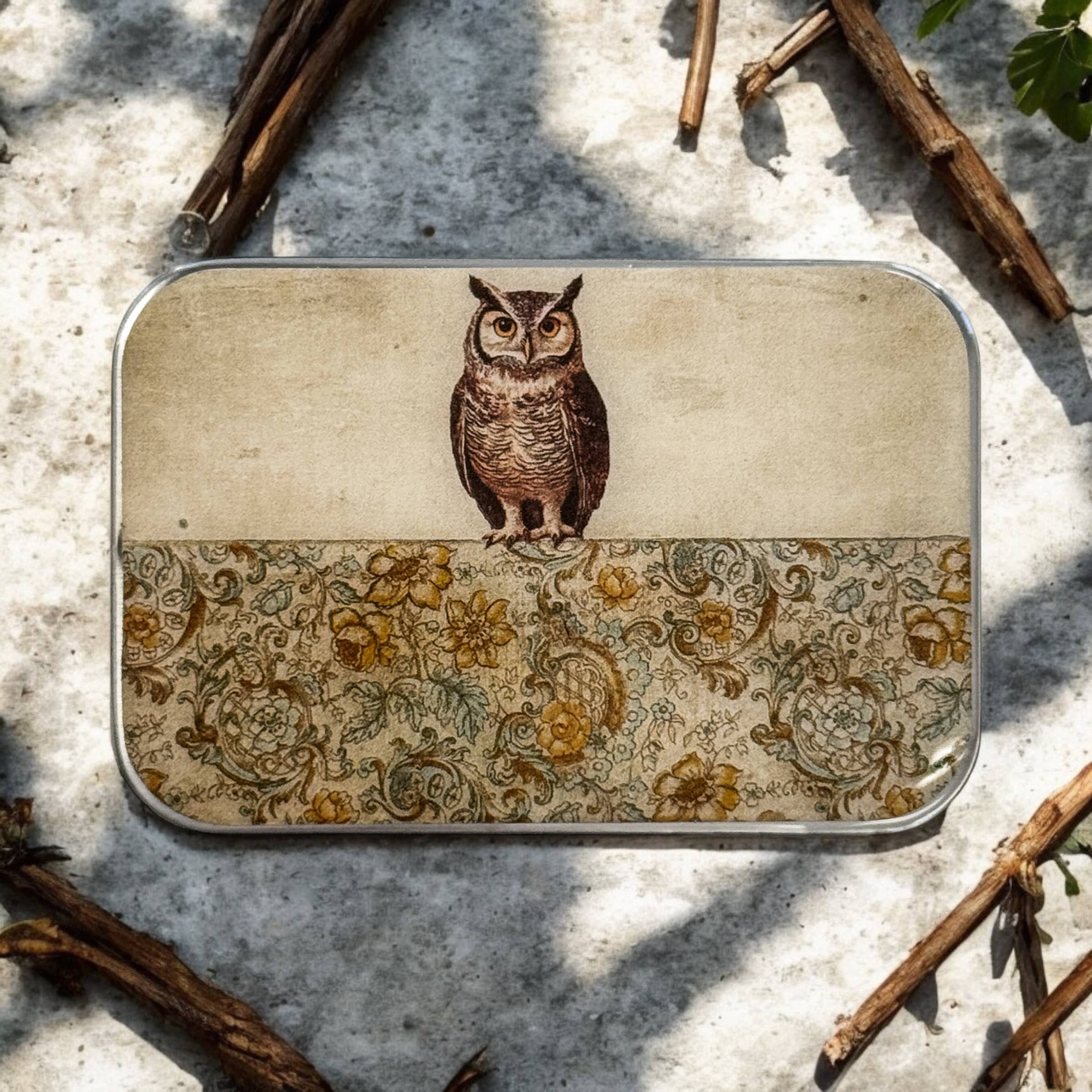 The Firefly Notes Owl Notions Tin features a vintage owl illustration on the lid and a floral pattern below. This rectangular tin is perfect for storing small items and makes a charming addition to any craft or sewing collection.