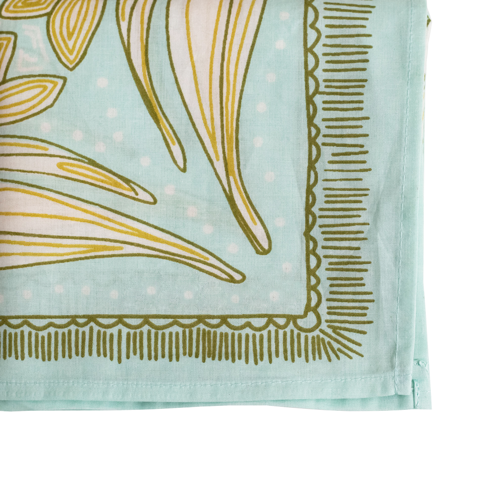 Close-up of the No. 012 Eliza Bandana by Handker Bandanas, featuring a light blue floral design with green and yellow abstract patterns, decorative border, visible edge stitching, and hand screen-printed on premium cotton.