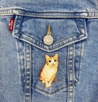 A Levis denim jacket pocket with a metal button features a Wholesale Applique Orange Tabby Cat embroidered iron on patch, showing a realistic kitten, sewn onto the pocket.