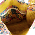 A close-up of the Calico Quilted Tote by Handker Bandanas reveals its colorful patchwork, yellow interior, inner zippered pocket, and a camera peeking out.