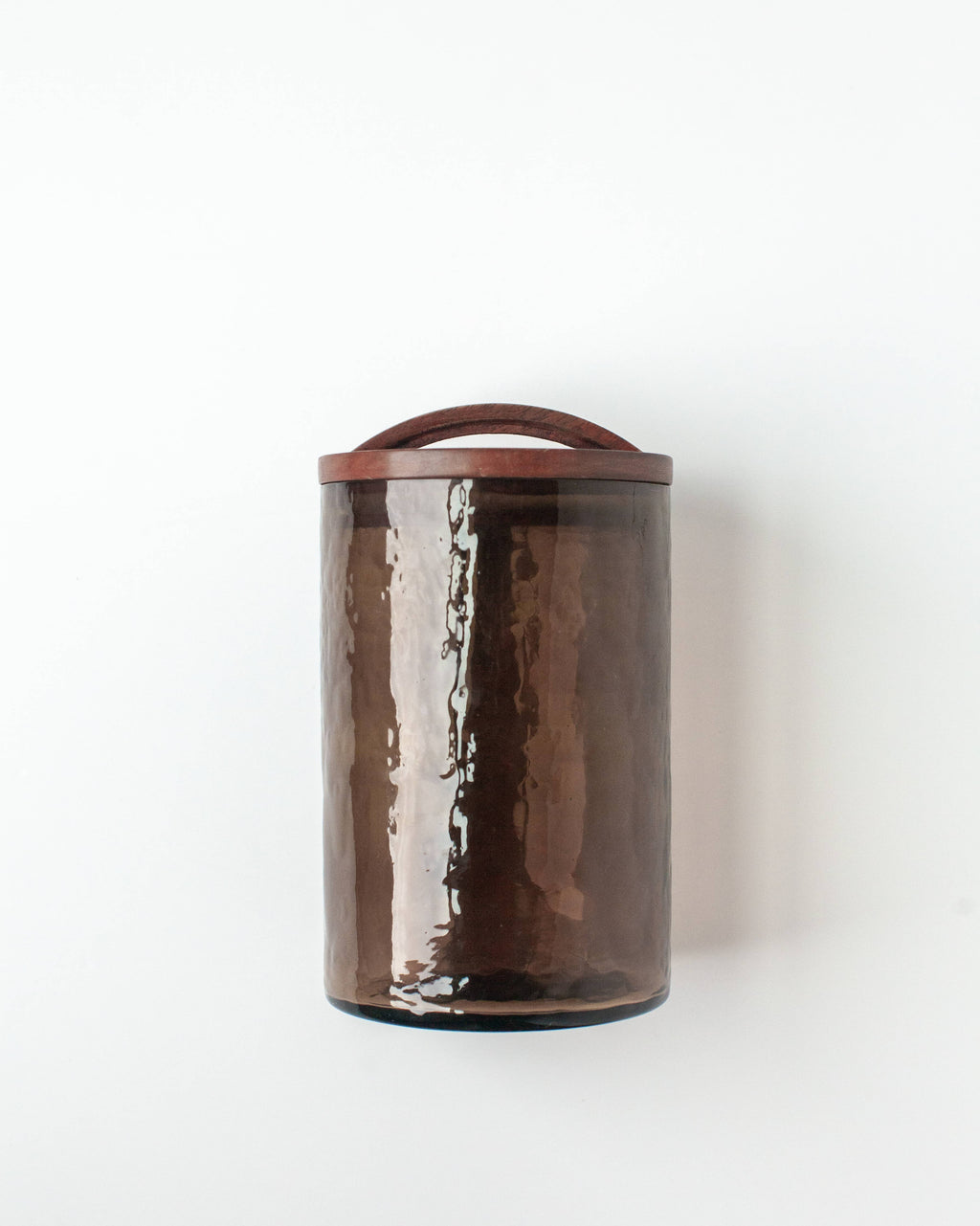 The Handblown Hammered Glass Canisters: Blush / Medium by Creative Women is a tall, cylindrical blush glass canister with a matching lid and curved handle, shown against a plain white background.