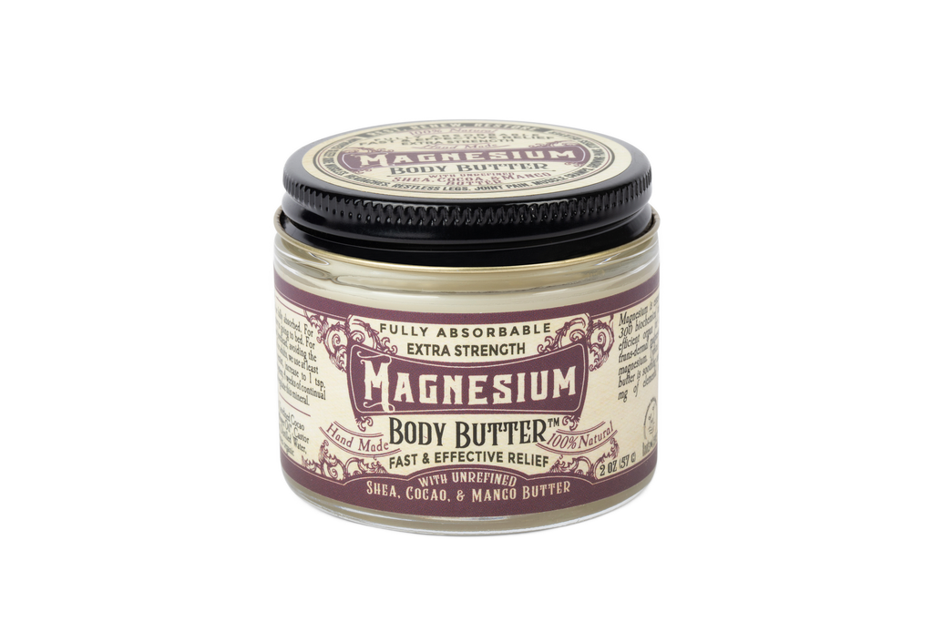 A glass jar of Roots And Leaves Magnesium Body Butter features extra strength, unrefined shea, cocoa, and mango butters for optimal magnesium absorption. The purple and cream labels on the lid and front are clearly visible.