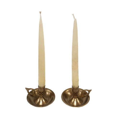 Two tall, cream-colored tapers are set in matching Brighton Bun Traveling Chambersticks by Madison Bay Co.—an elegant antique revival with small handles, displayed on a plain white background.
