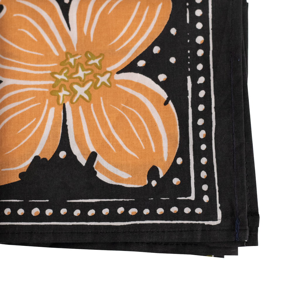 The No. 046 Amy Bandana by Handker Bandanas is a folded cotton accessory featuring a bold orange dogwood flower with yellow accents on a black background, bordered by white dots and lines.