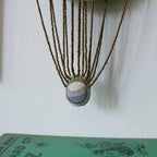 The Skippy Cotton "Wonderful Wizard / Balloon, Oz Wallhanging" features a fabric ball suspended by beaded strings above a green book, creating whimsical embroidered wall art or an ornament.
