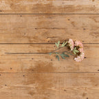 The Ragon House 25" Pink Faux Hydrangea Spray, featuring pink and white blooms with green leaves, is displayed horizontally on a rustic wooden surface.