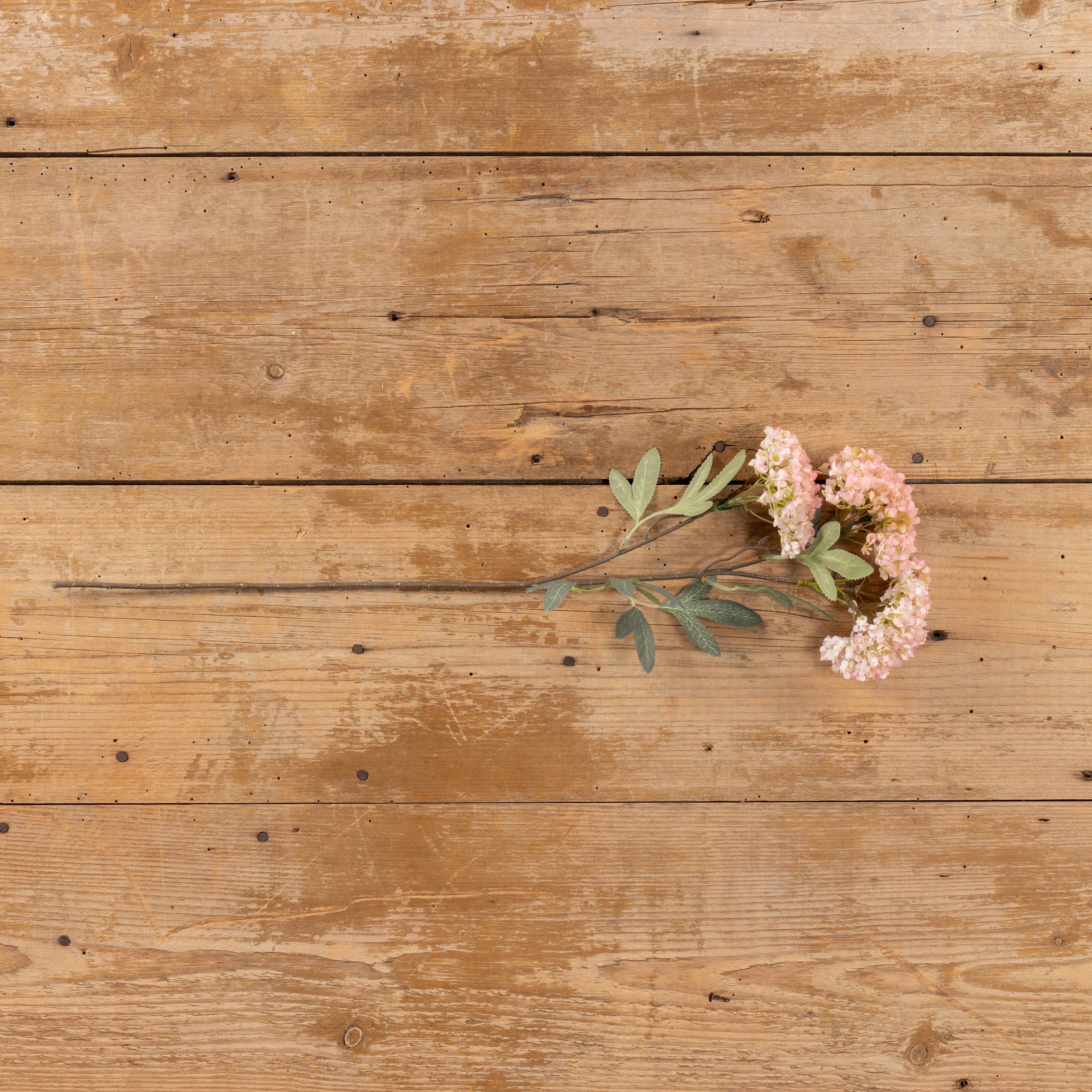 The Ragon House 25" Pink Faux Hydrangea Spray, featuring pink and white blooms with green leaves, is displayed horizontally on a rustic wooden surface.