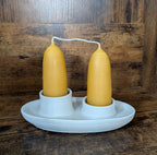A pair of British-style, hand-dipped Beeswax Stubby Candles by Yarrow Bone Farmstead stand upright in a white ceramic holder with two circular slots, set against a wooden background.