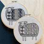 The Sweater Weather Sheep Complete Embroidery Kit by Hook, Line & Tinker features two hoops with sheep stitched in black thread, each with geometric patterned wool—an adorable addition to any embroidery or craft kit.