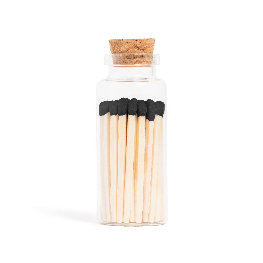 Enlighten the Occasion Black Matches in Corked Vial: Sleek black wooden matches with bold black tips are displayed upright in a small glass bottle with a cork stopper against a white background.