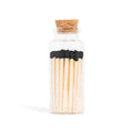 Enlighten the Occasion Black Matches in Corked Vial: Sleek black wooden matches with bold black tips are displayed upright in a small glass bottle with a cork stopper against a white background.
