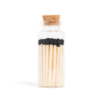Enlighten the Occasion Black Matches in Corked Vial: Sleek black wooden matches with bold black tips are displayed upright in a small glass bottle with a cork stopper against a white background.