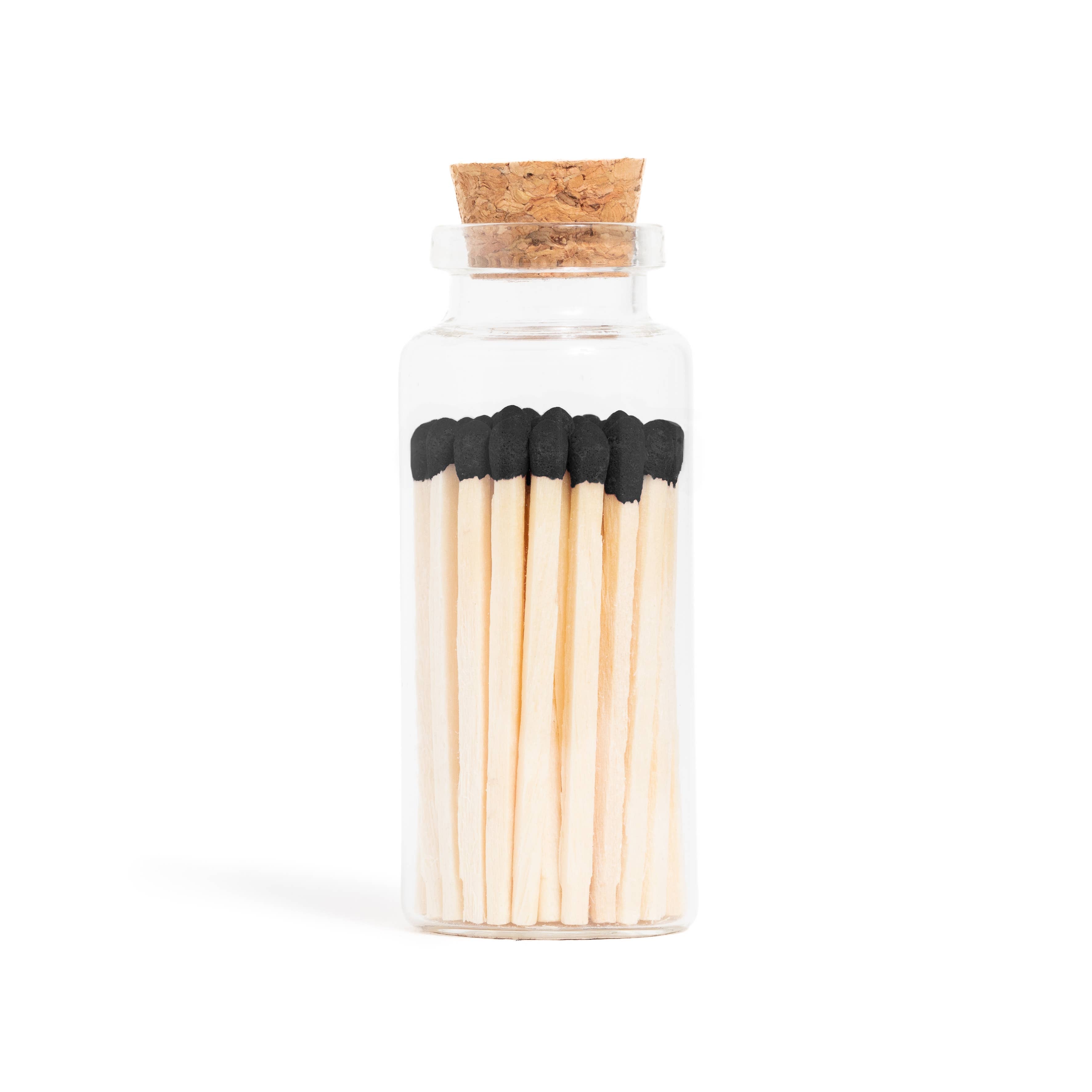 Enlighten the Occasion Black Matches in Corked Vial: Sleek black wooden matches with bold black tips are displayed upright in a small glass bottle with a cork stopper against a white background.