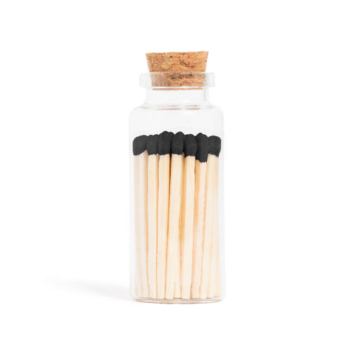 Enlighten the Occasion Black Matches in Corked Vial: Sleek black wooden matches with bold black tips are displayed upright in a small glass bottle with a cork stopper against a white background.