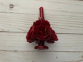 A deep red, floral-shaped Wine Oaxaca Marigold Day of the Dead Candle by Viva Greetings resting on a wooden surface.