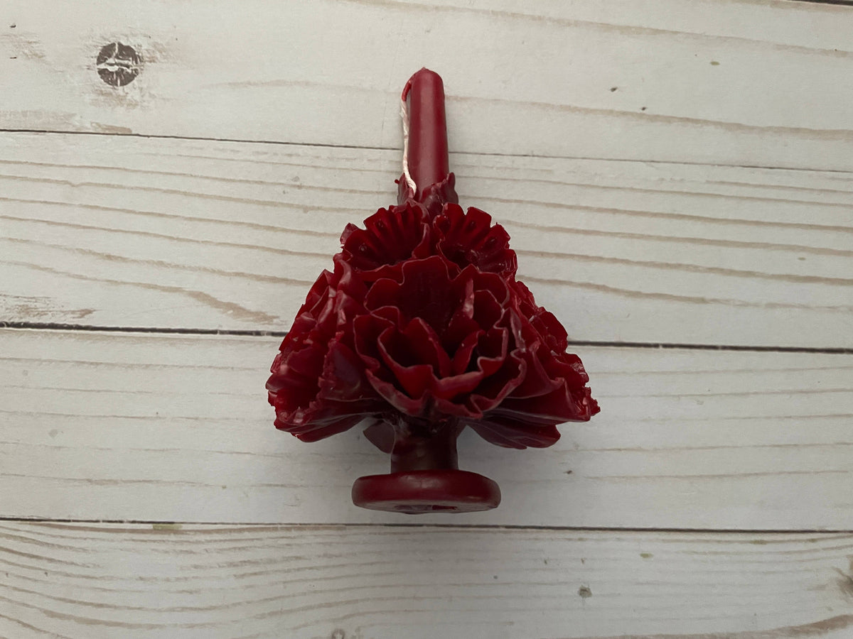 A deep red, floral-shaped Wine Oaxaca Marigold Day of the Dead Candle by Viva Greetings resting on a wooden surface.