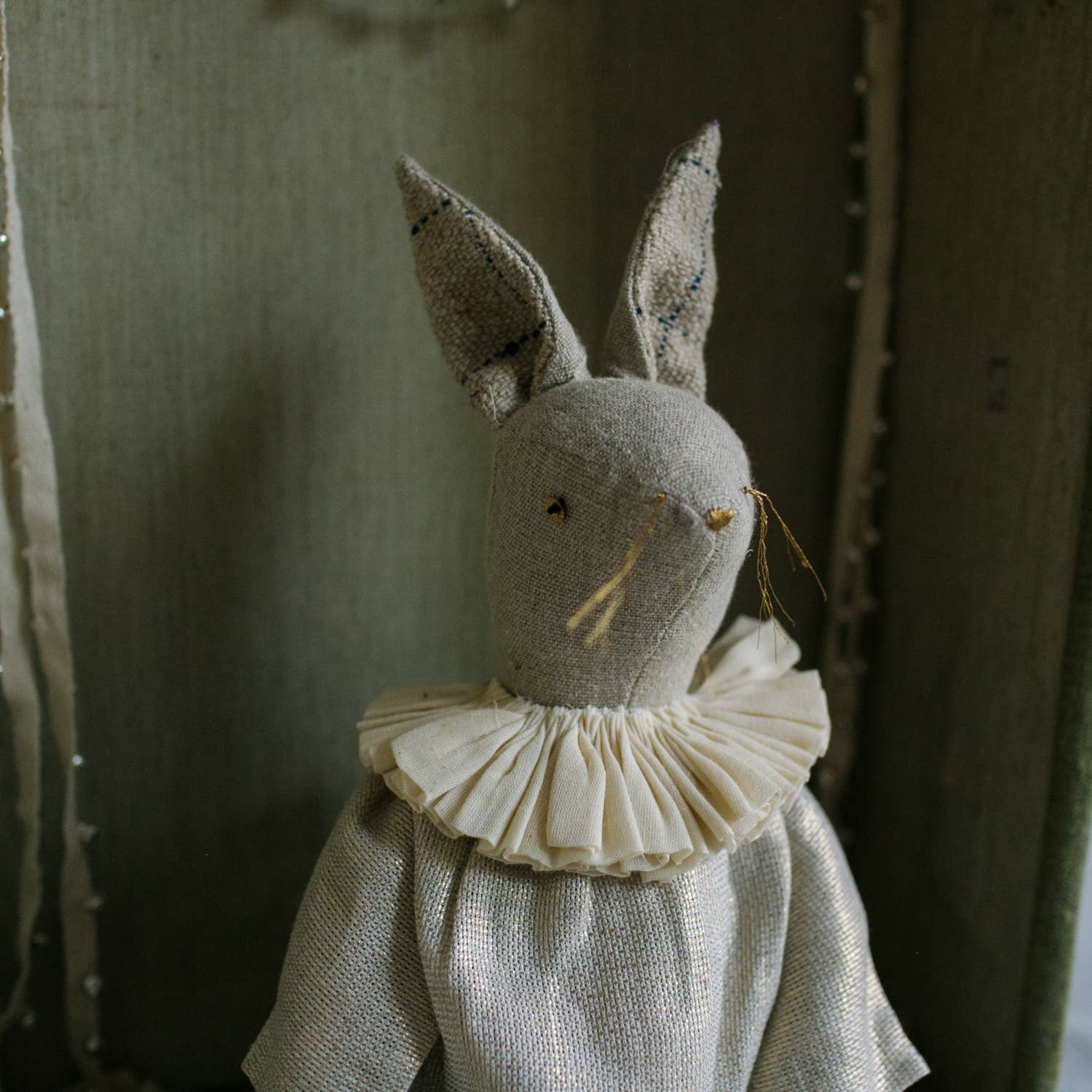 The Skippy Cotton Ruffle Bun Ragdoll is a cotton-filled art doll in a charming cotton dress, with long ears, embroidered face, ruffled collar, and delicate hand-stitched details, set against a rustic background.