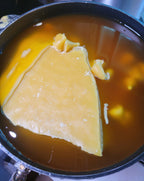 A large slab of pure beeswax melts into golden liquid with floating chunks—ideal for crafting Yarrow Bone Farmstead's 7 inch Pair Hand-Dipped Pure Beeswax Tapers.