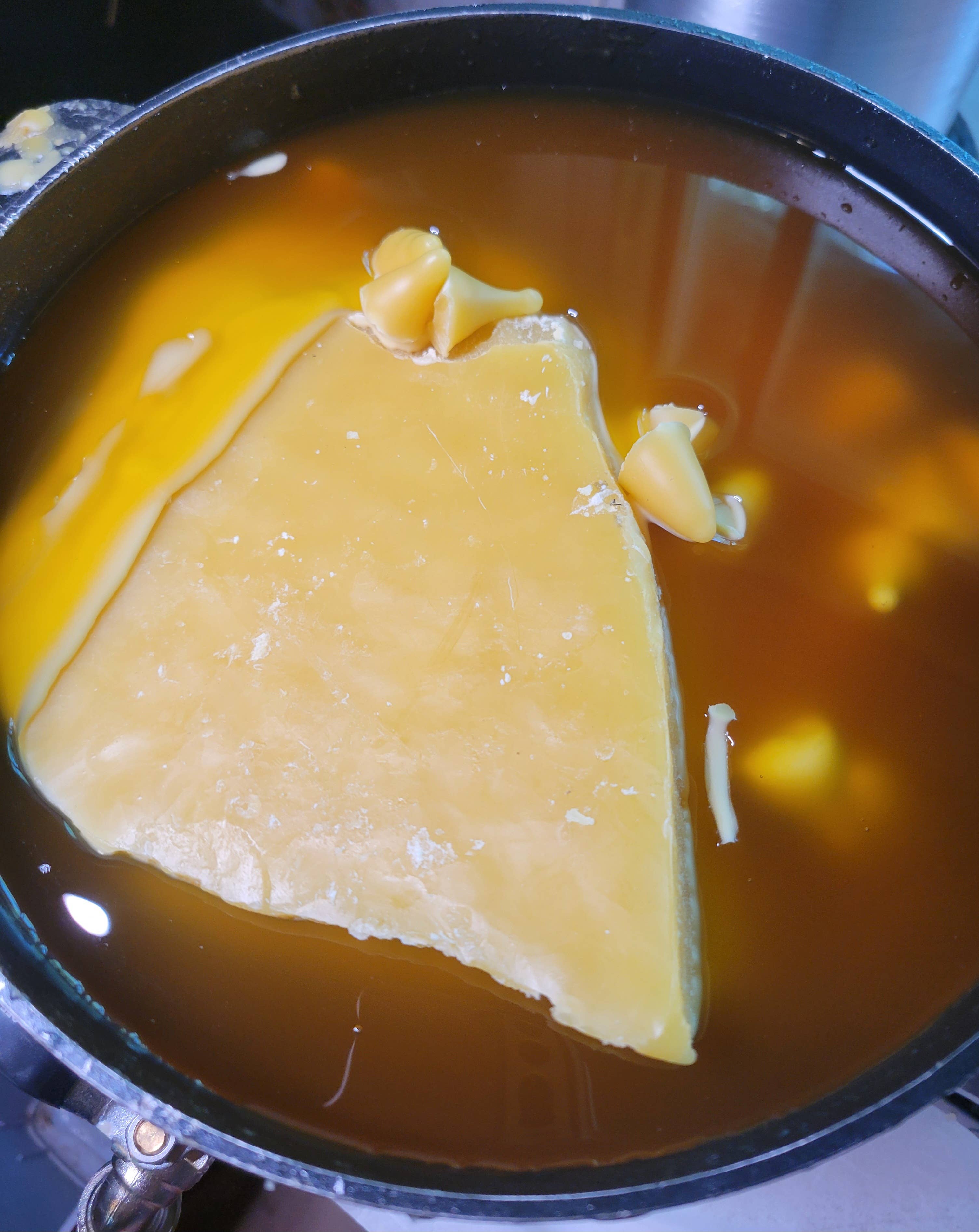 A large slab of pure beeswax melts into golden liquid with floating chunks—ideal for crafting Yarrow Bone Farmstead's 7 inch Pair Hand-Dipped Pure Beeswax Tapers.