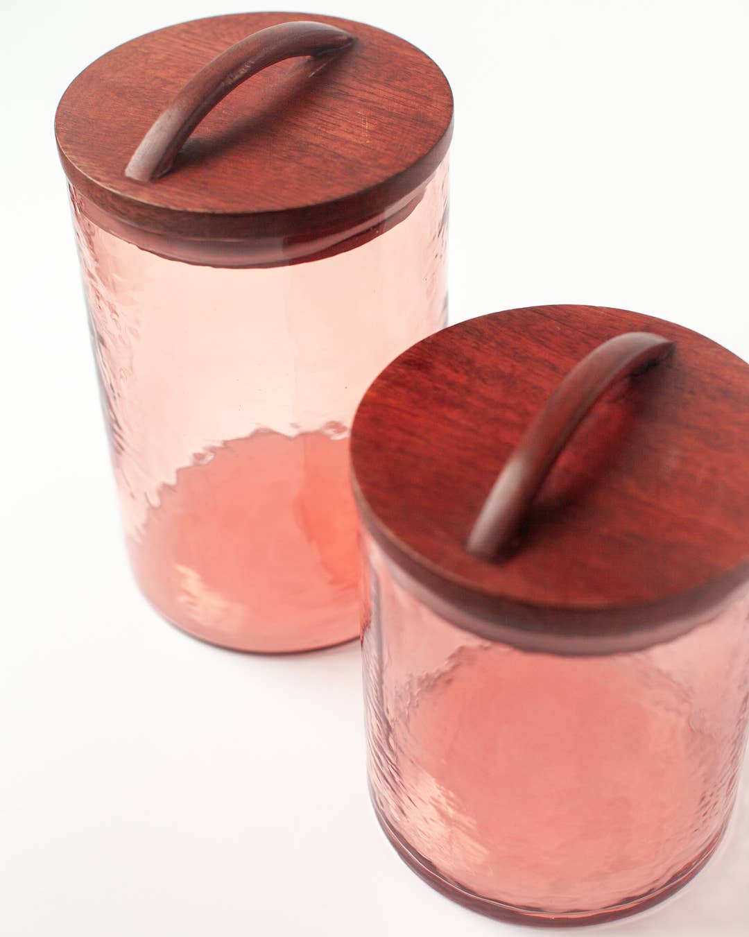 Two Handblown Hammered Glass Canisters: Smoke / Medium by Creative Women with hand-carved wooden lids and curved handles, displayed on a white surface.