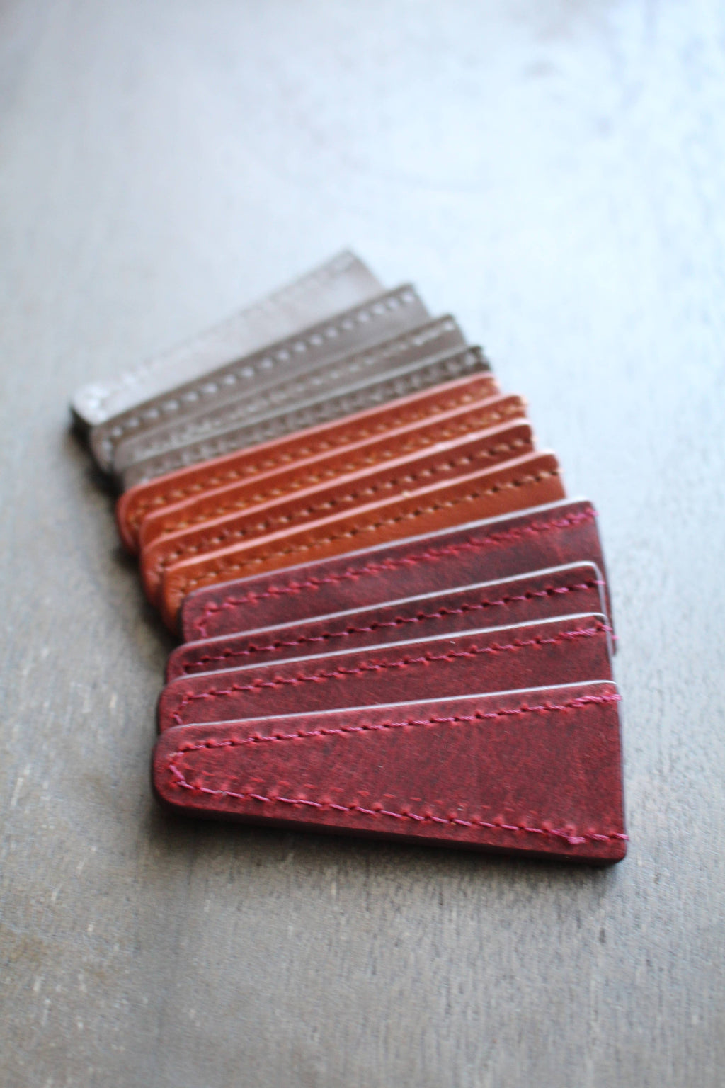 NNK Press Leather Scissor Sheaths in red, brown, orange, and gray are arranged diagonally on a wooden surface—ideal for storing embroidery accessories or protecting your scissors in style.