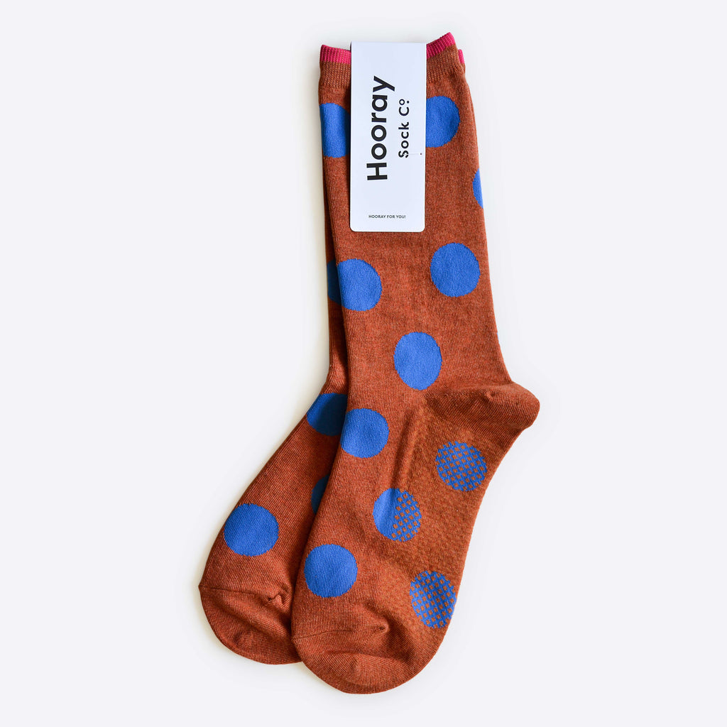 The Hooray Sock Co. Panhandle Polka Dot Crew Socks feature a brown base with large blue polka dots, crew length, and a comfortable cotton-spandex blend, shown flat with the brand label attached at the top. Unisex design.