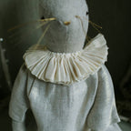A close-up of the Skippy Cotton Ruffle Bun Ragdoll, a handmade linen art doll with stitched features, cotton filling, thin whiskers, and a cotton dress adorned with a ruffled white collar.