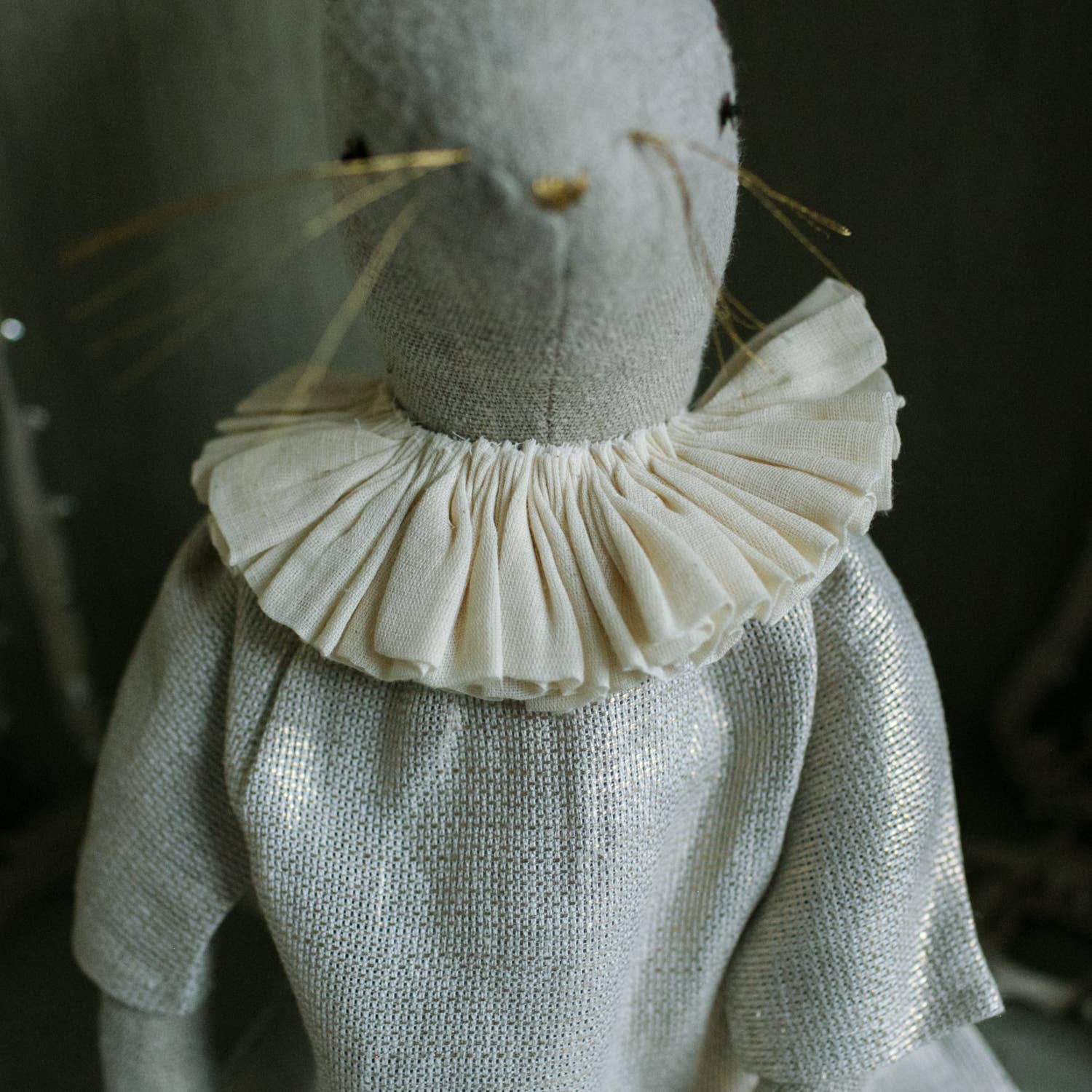 A close-up of the Skippy Cotton Ruffle Bun Ragdoll, a handmade linen art doll with stitched features, cotton filling, thin whiskers, and a cotton dress adorned with a ruffled white collar.