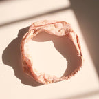 The Horses Cotton Headband by Handker Bandanas features hand screen-printed Pink Mist Horses line art on pink fabric, displayed in a loose circle on a sunlit white surface with soft shadows.