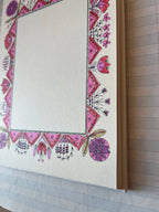 Parcel’s Colorful Folk Frame set includes 8 notebooks with blank pages framed by pink, purple, and red floral and geometric designs on quality cardstock, each notebook resting atop a lined sheet of paper.